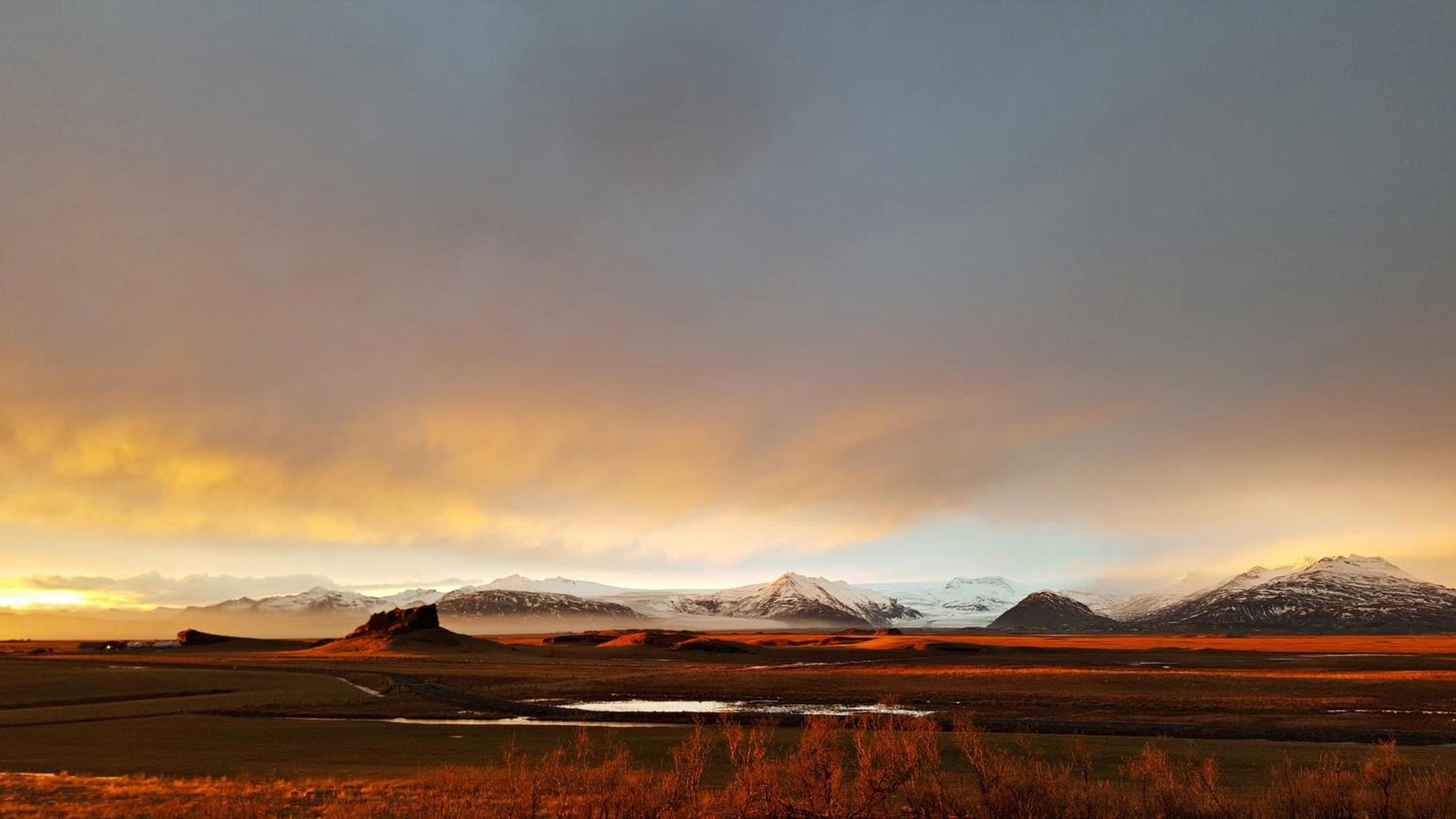 Low sun across the Mýrar lowlands below Nýpugarðar, with outlet glaciers and snow-covered peaks on the horizon