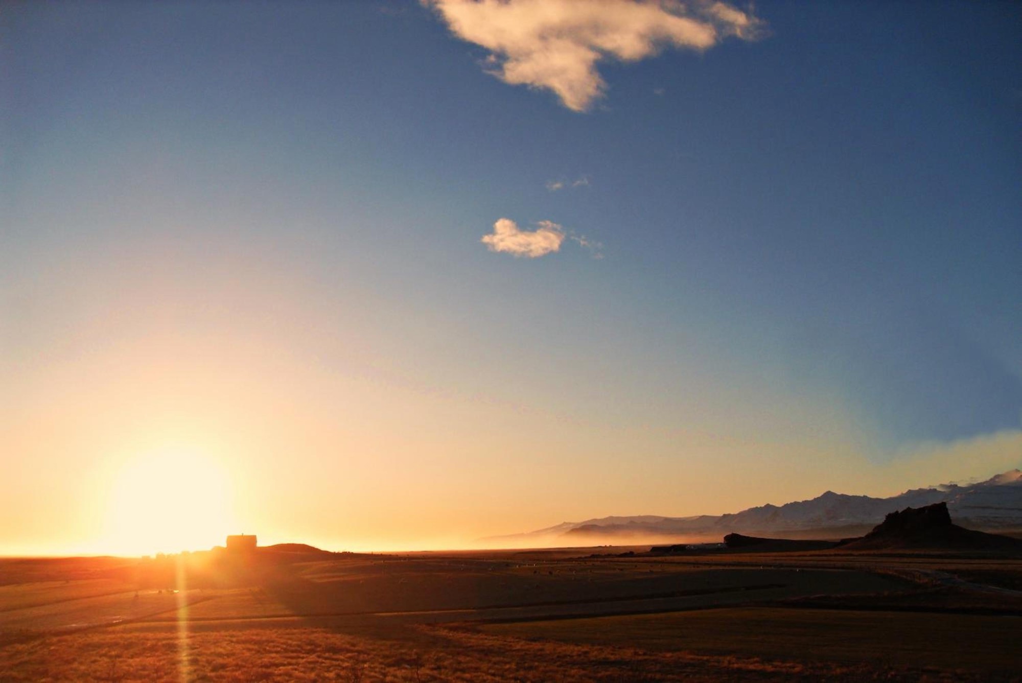 The sun setting over the open fields at Nýpugarðar, with the mountains dark on the horizon