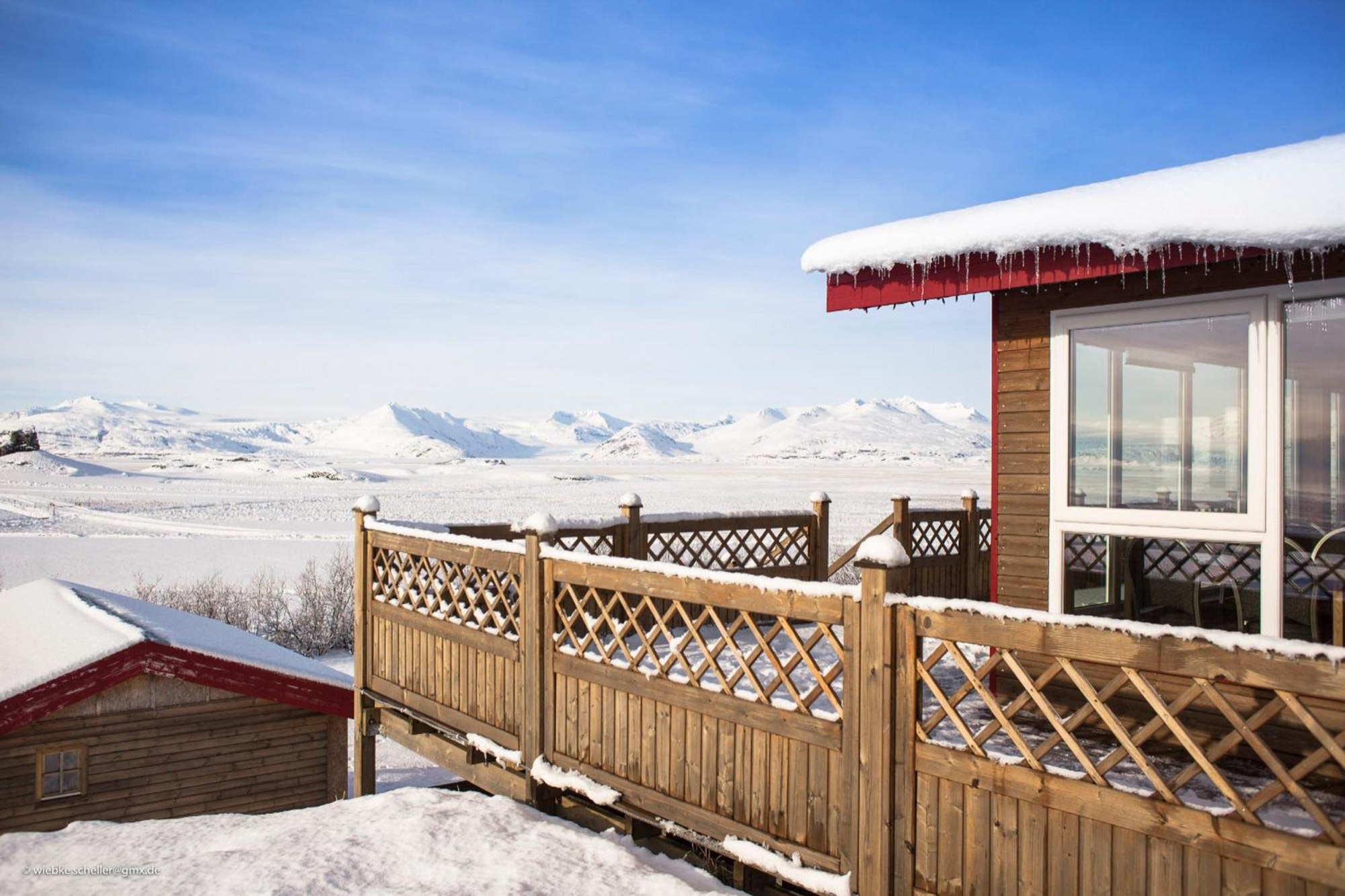The guesthouse at Nýpugarðar in deep winter snow, with the deck and large windows facing the mountains