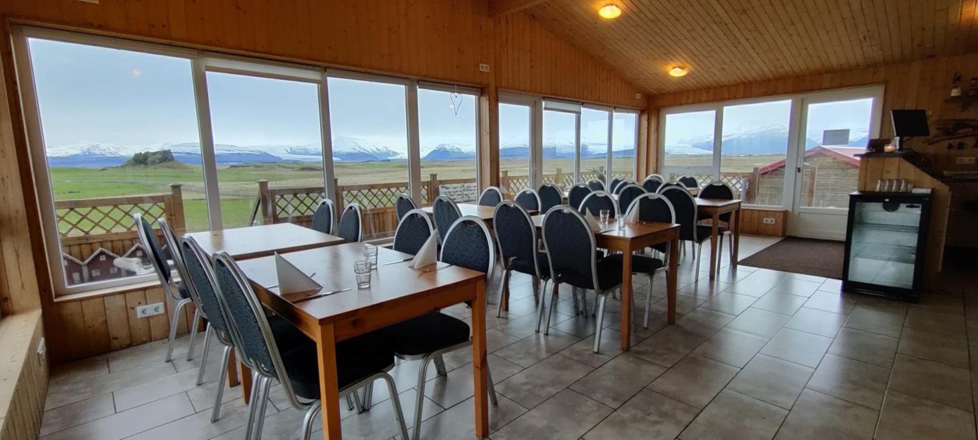 The dining room at Nýpugarðar, with tables set beside full-height windows facing the glacier