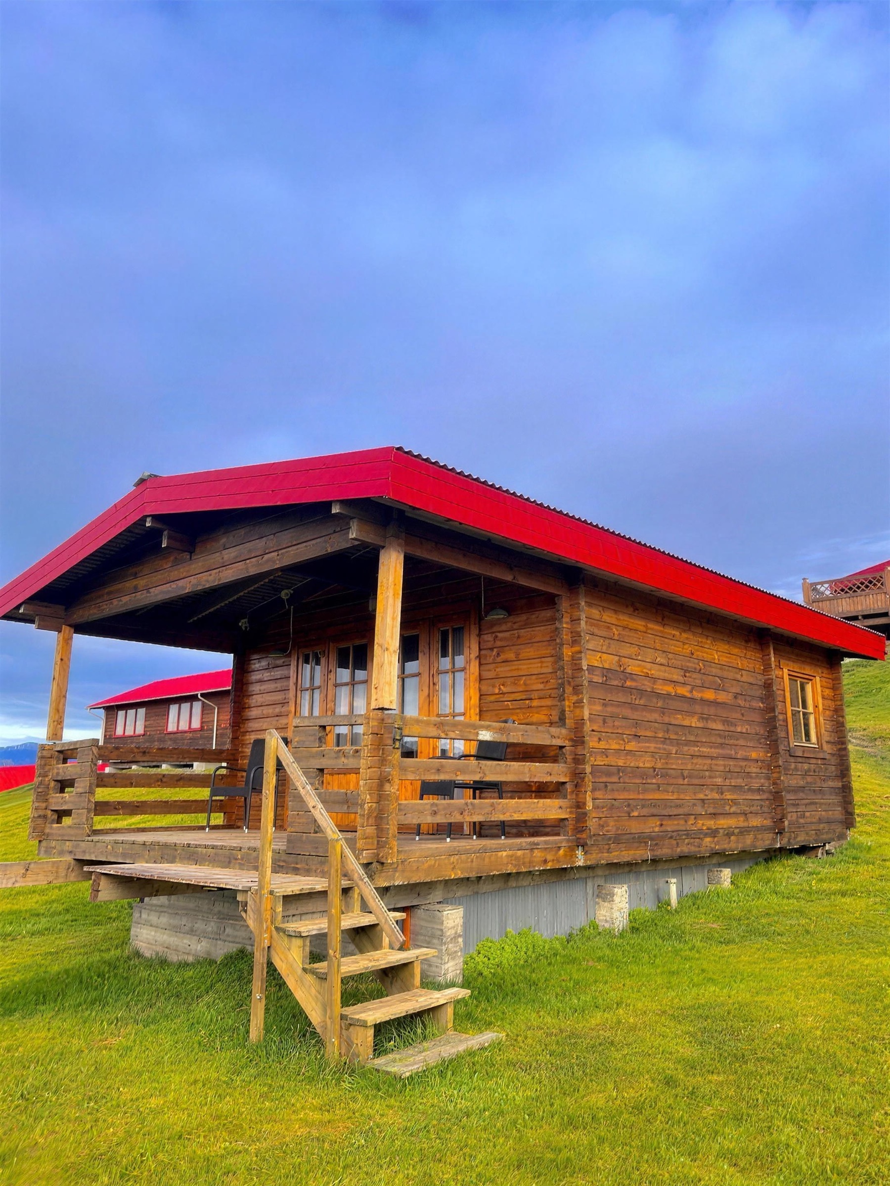 The family cottage at Nýpugarðar, red roof and a timber porch, standing on the grass